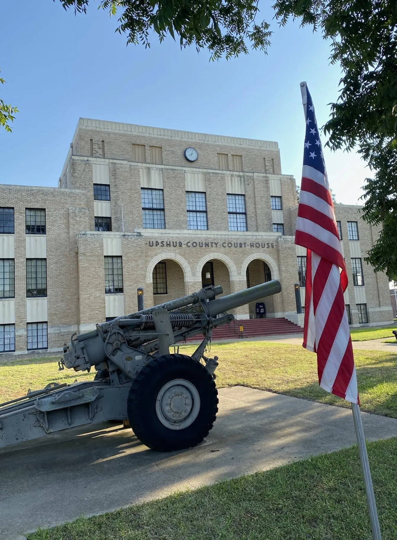 A courthouse with an American flag and a cannon on the lawn.