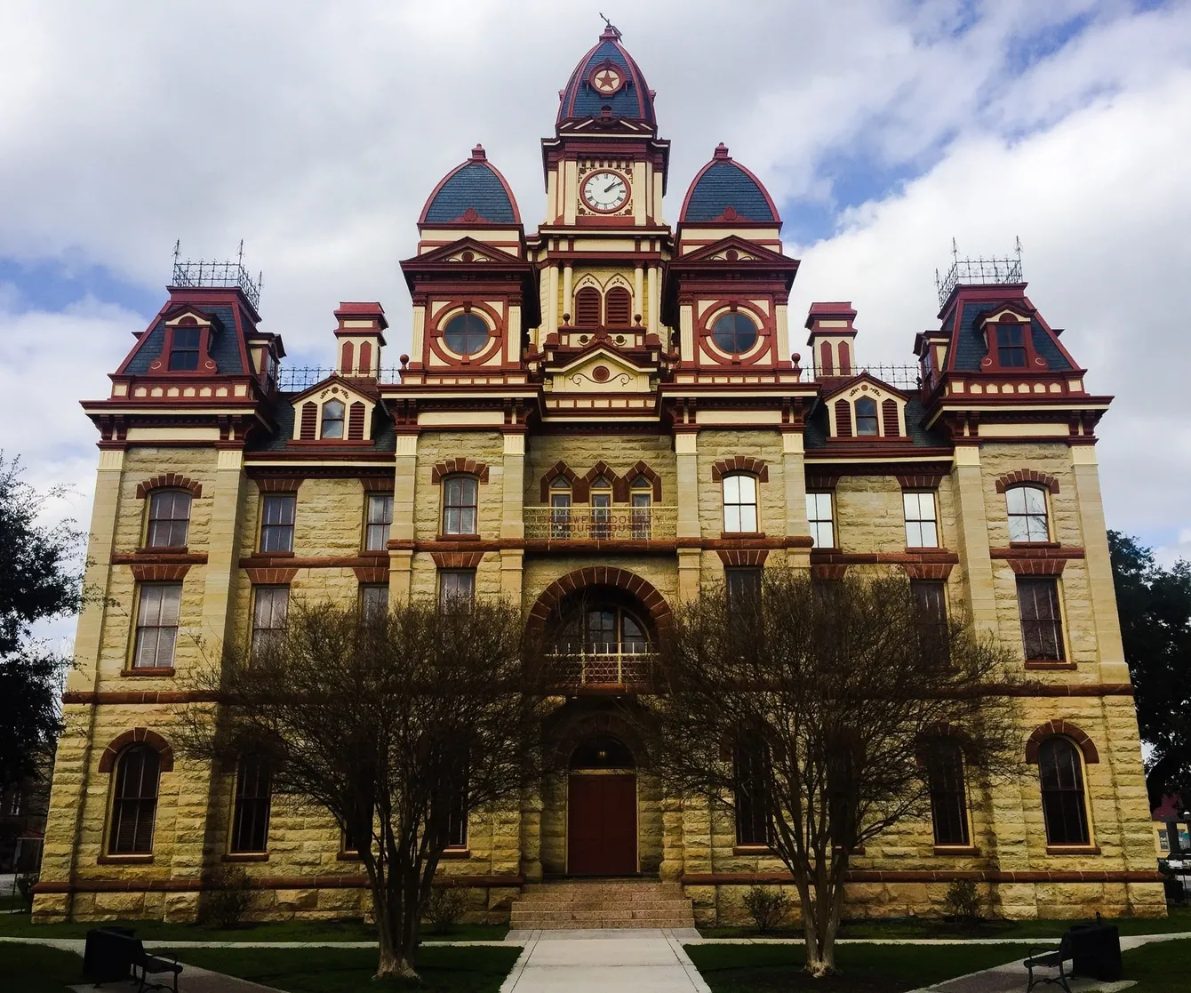 Historic stone courthouse with clock tower and red accents, under cloudy sky.