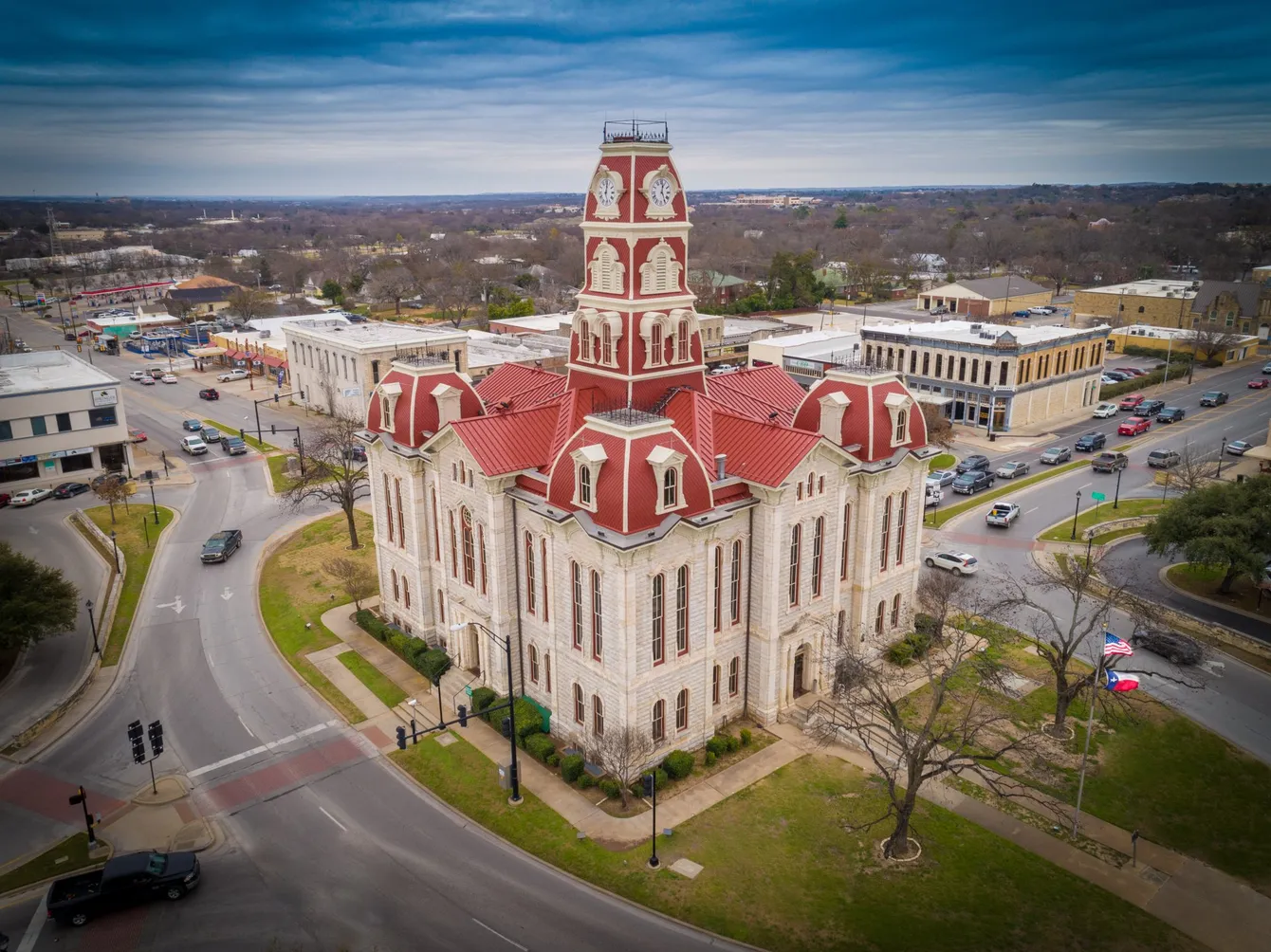 Historic limestone courthouse with red roof, surrounded by roads and buildings in a town.
